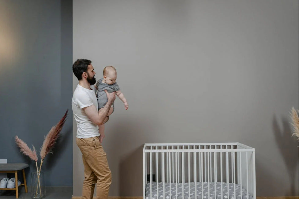 father holding baby next to crib