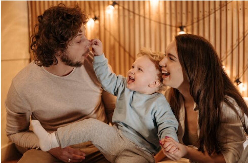 A baby plays with his dad’s face while sitting next to his mom